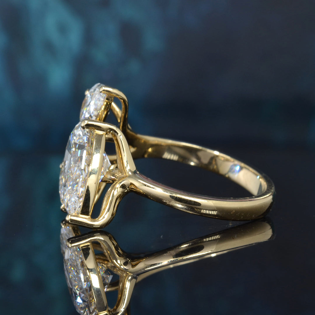 A yellow gold ring with a large oval-cut diamond and smaller side stones, shown in a close-up studio shot on a dark reflective surface.