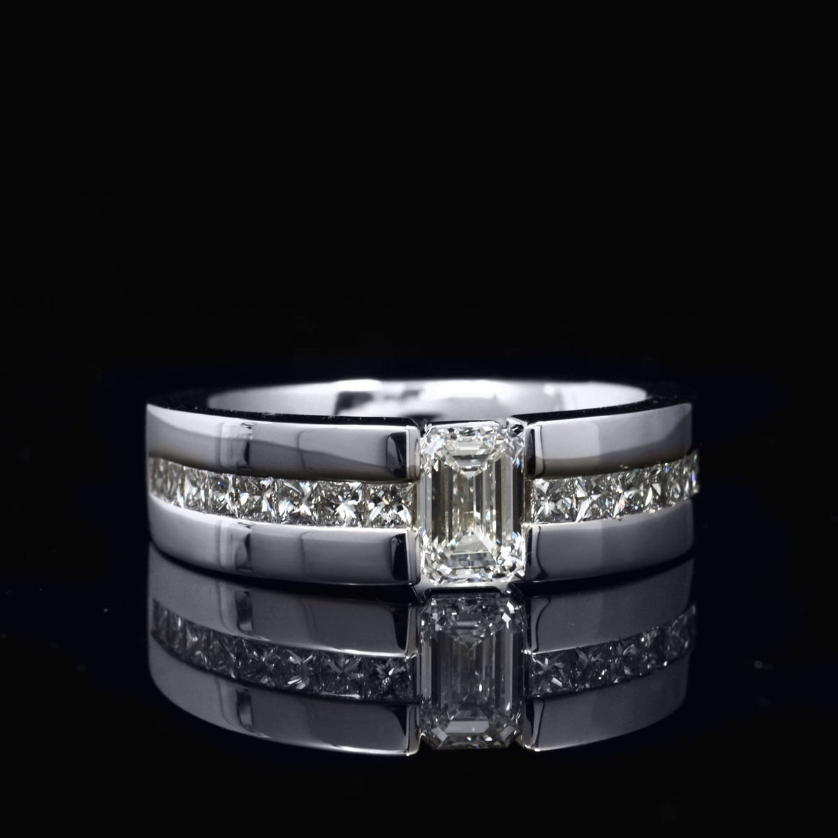 Diamond ring with a central emerald cut diamond and smaller princess cut diamonds on a black background