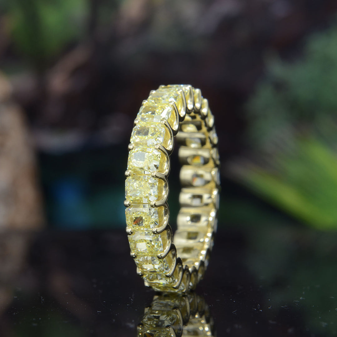 Gold eternity bandt with yellow diamonds on a brown surface on a reflective surface with a blurred natural background