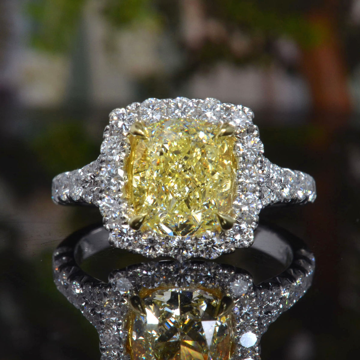 Diamond ring with a yellow center stone and gold surround on a reflective surface