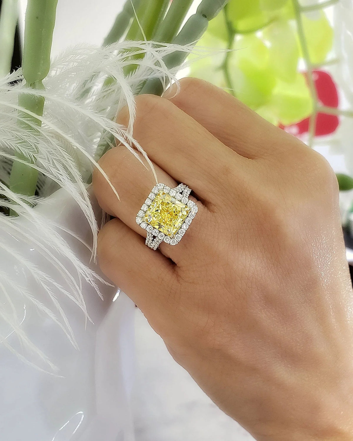 Square radiant cut yellow diamond set at the center of a halo split‑shank ring, crafted in white gold and secured with yellow‑gold prongs on model's ring finger