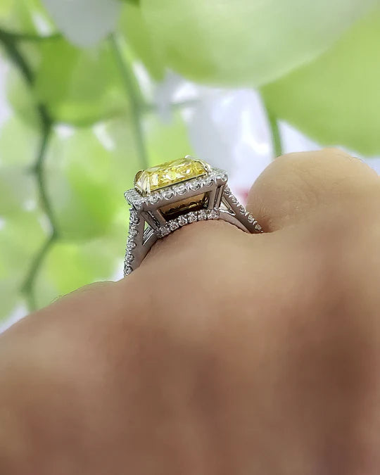 square radiant cut yellow diamond set at the center of a halo split‑shank ring, crafted in white gold and secured with yellow‑gold prongs on model's finger side profile