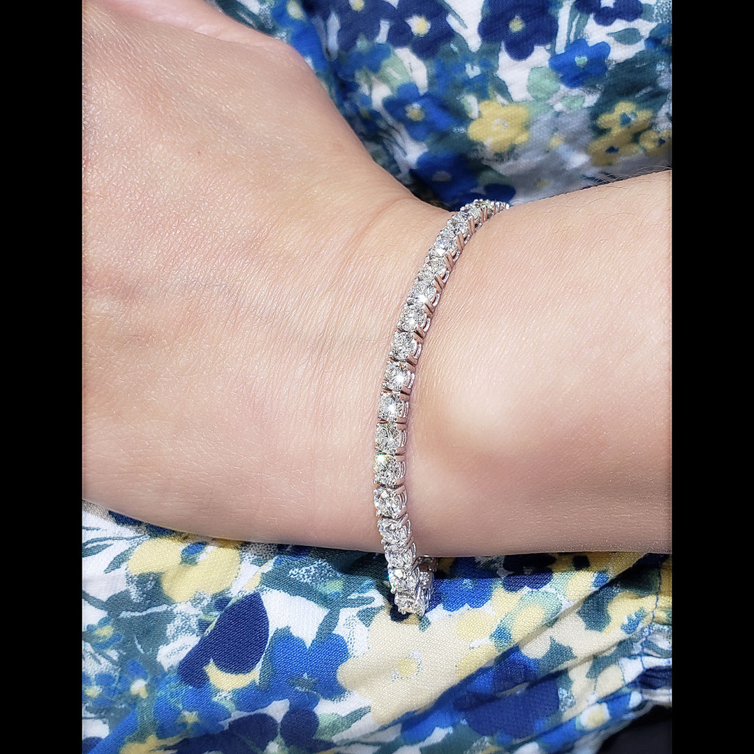 A close-up of a person's wrist wearing a white gold tennis bracelet with clear stones, set against a blue and yellow floral patterned garment.