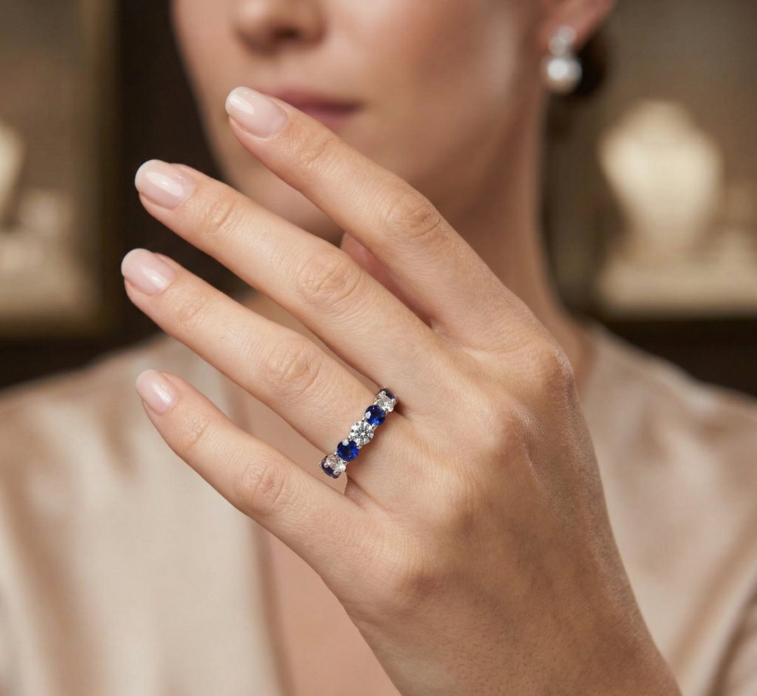 Close-up of a hand wearing a eternity band with alternating white diamonds and blue sapphire, blurred background