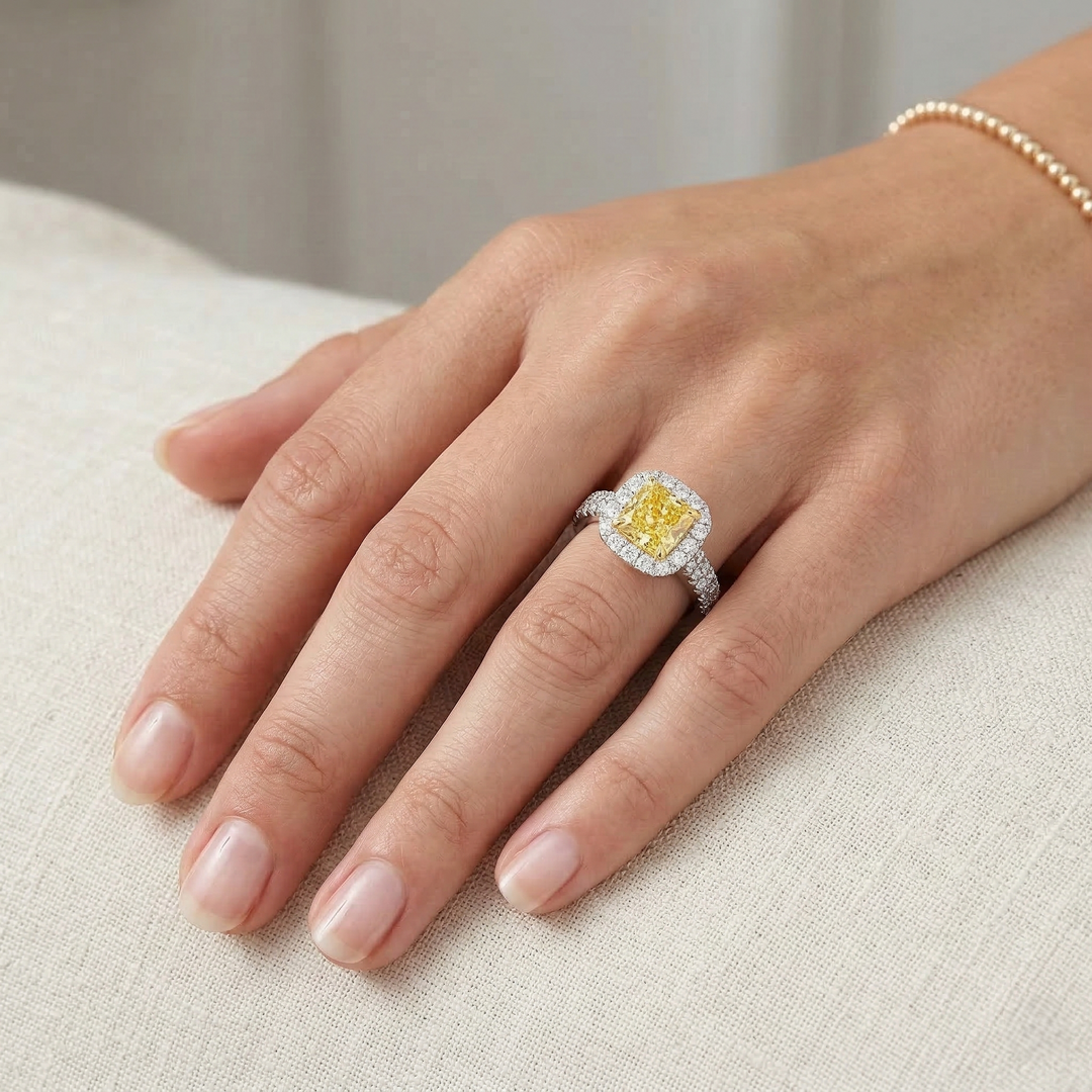 Hand wearing a ring with a yellow diamond on a neutral background