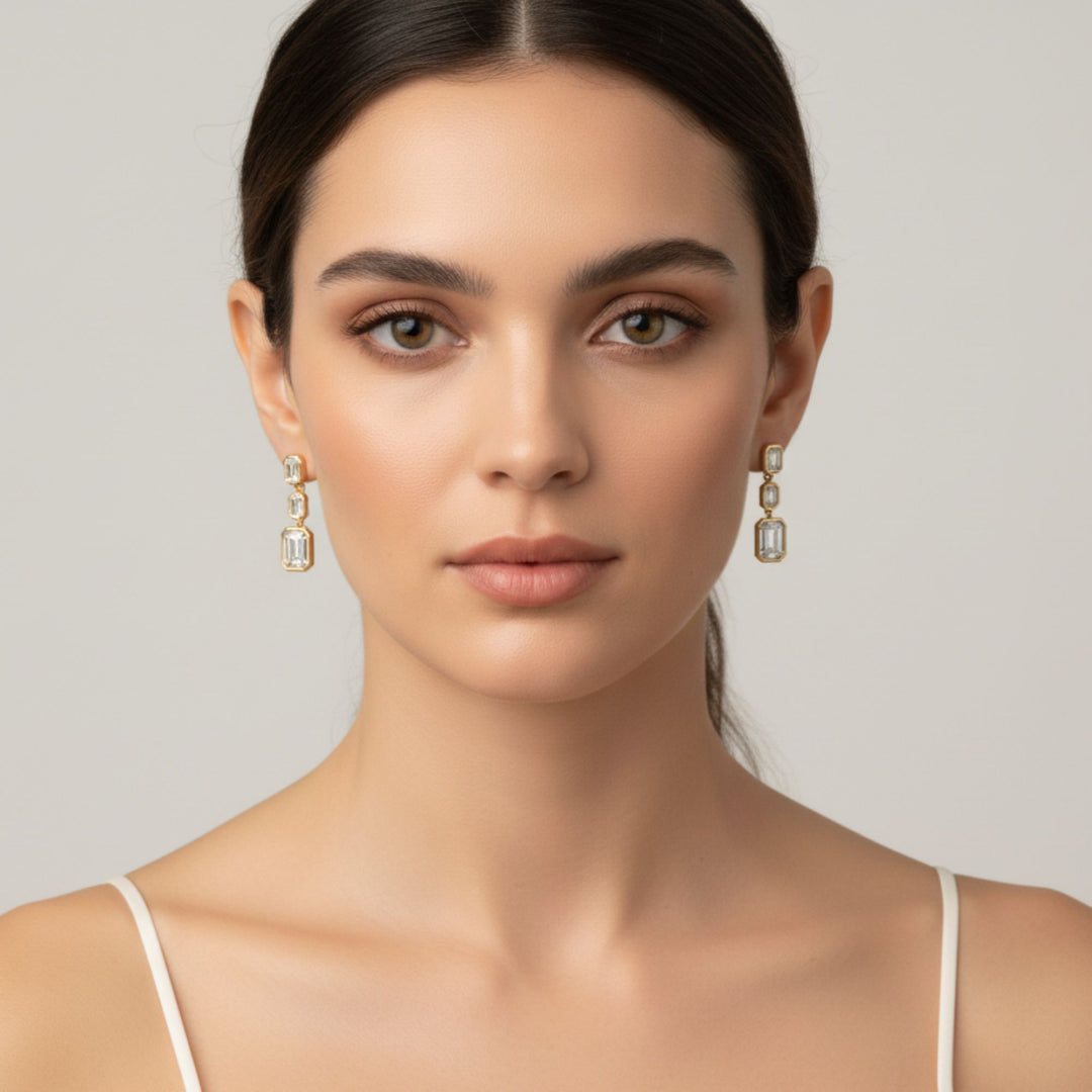 3 Emerald cut diamond dangling bezel set earrings in yellow gold worn by a lady model.