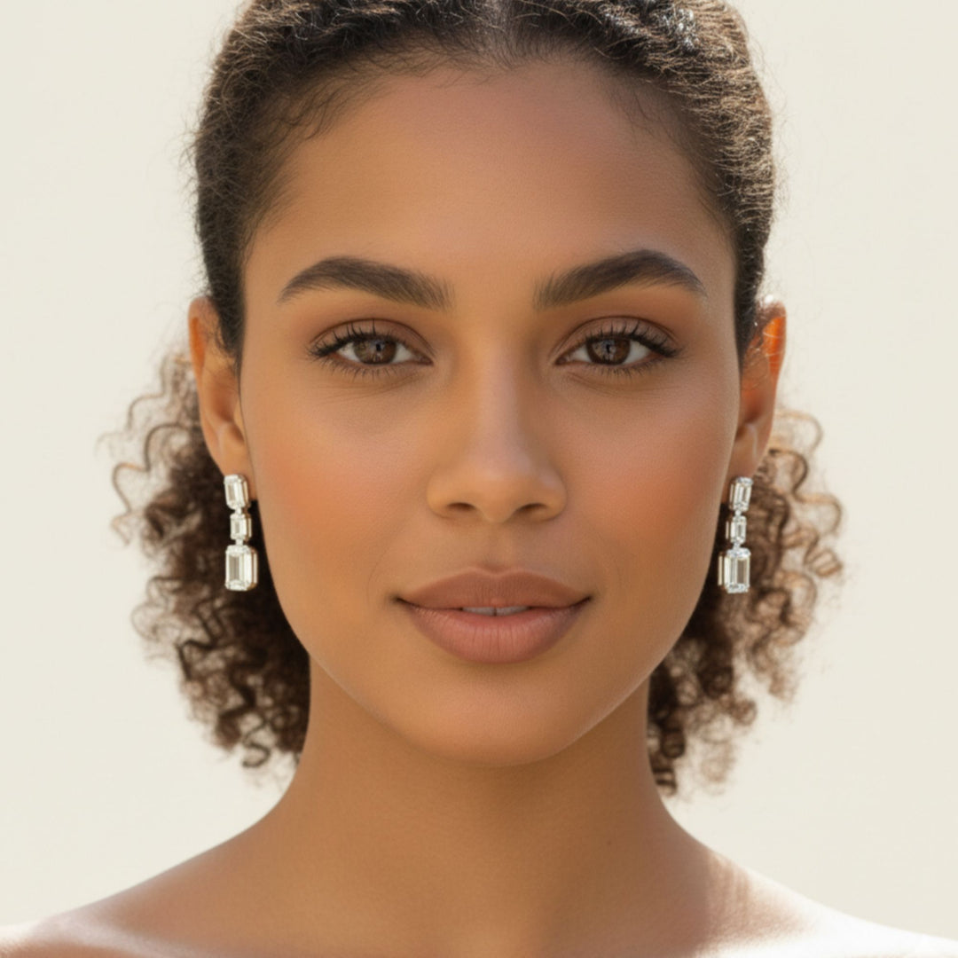 3 Emerald cut diamond dangling bezel set earrings in yellow gold worn by a lady model.