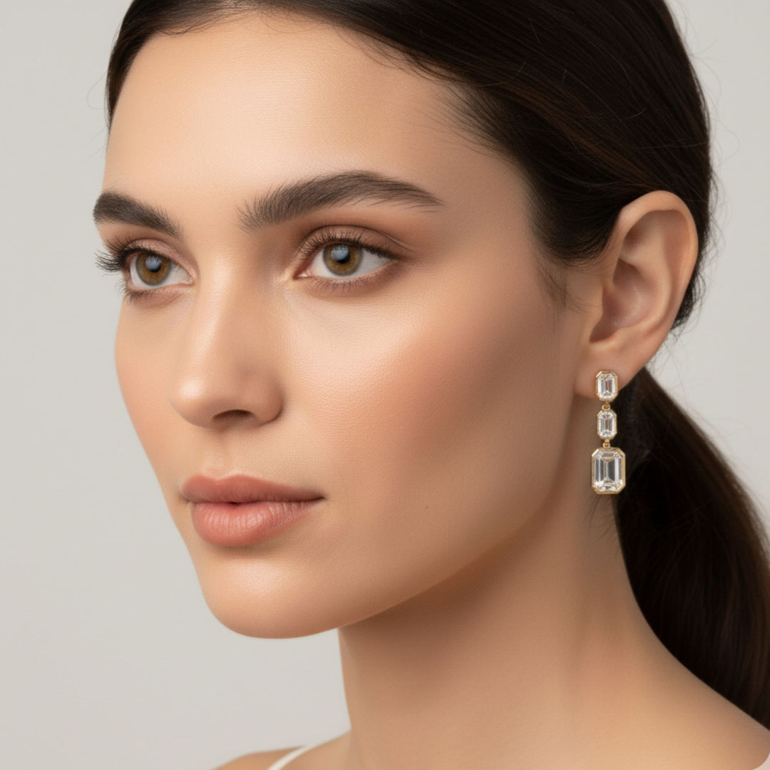 3 Emerald cut diamond dangling bezel set earrings in yellow gold worn by a lady model.