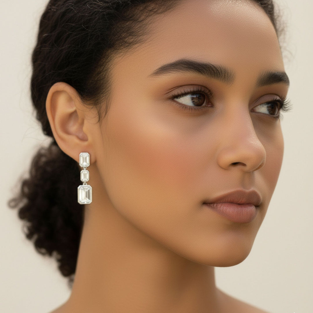 3 Emerald cut diamond dangling bezel set earrings in white gold worn by a lady model.