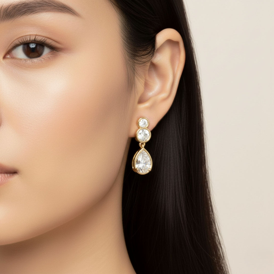 Pear & Round Diamond Bezel Set Dangling Earrings in yellow gold worn by a lady model