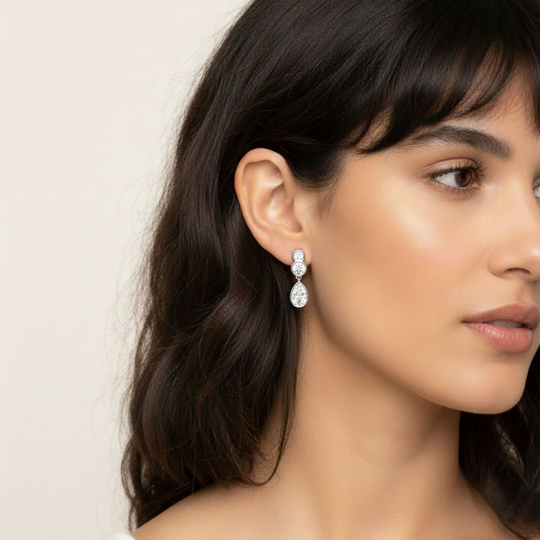 Pear & Round Diamond Bezel Set Dangling Earrings in white gold worn by a lady model