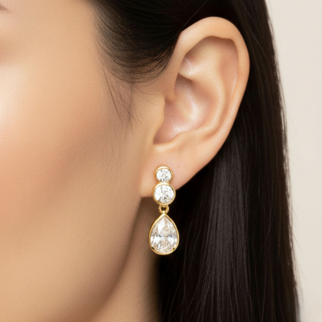 Pear & Round Diamond Bezel Set Dangling Earrings in yellow gold worn by a lady model