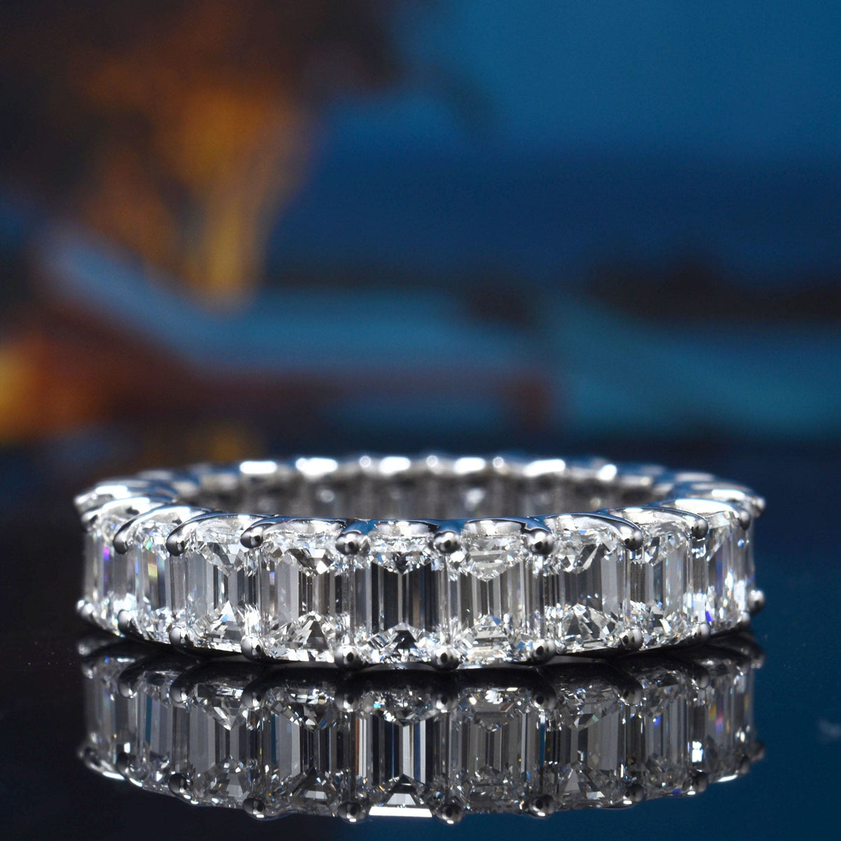 Diamond ring with emerald cut stones on a reflective surface with a blurred background