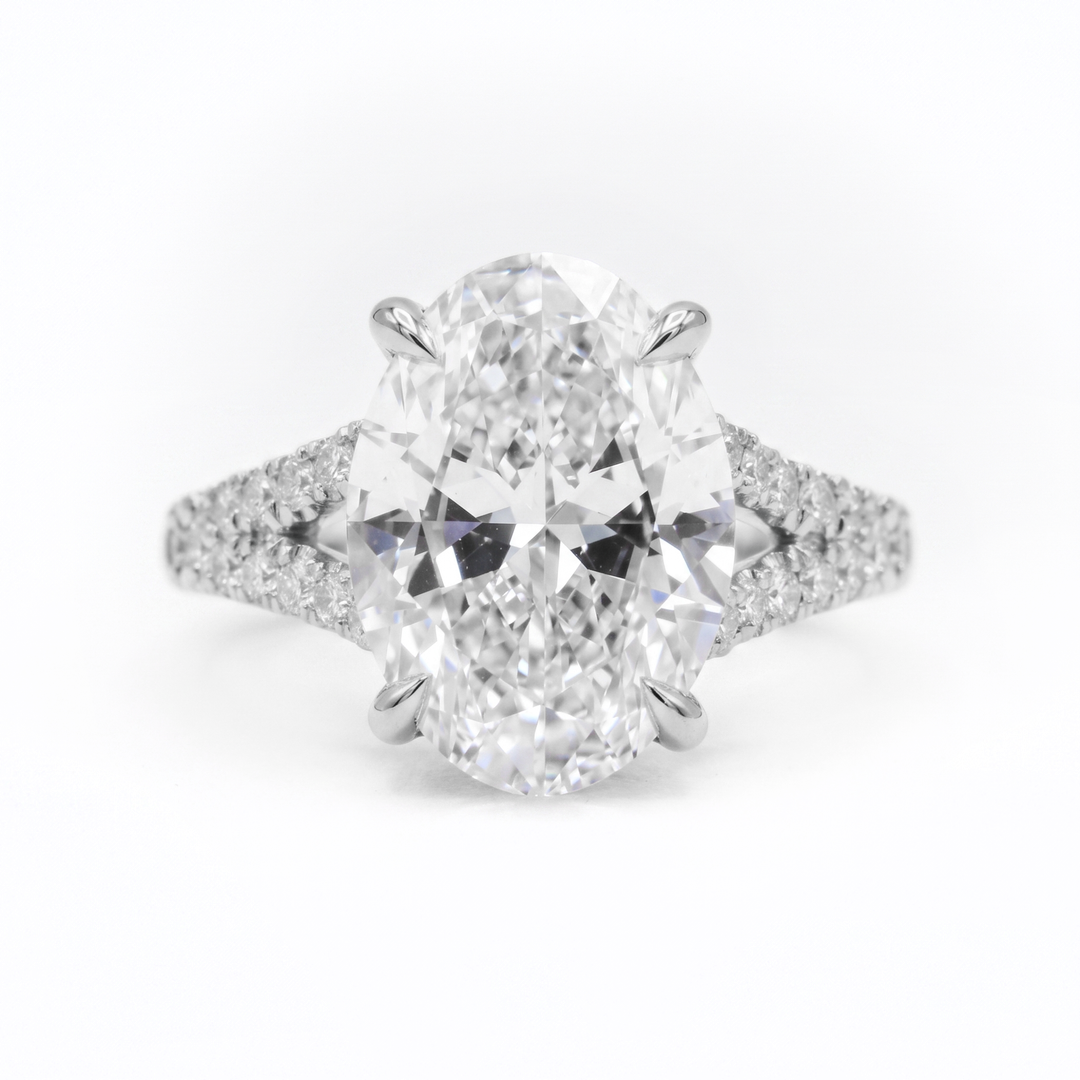 An oval-cut diamond engagement ring with a brilliant solitaire center stone and pavé-set diamond shoulders on a white background.