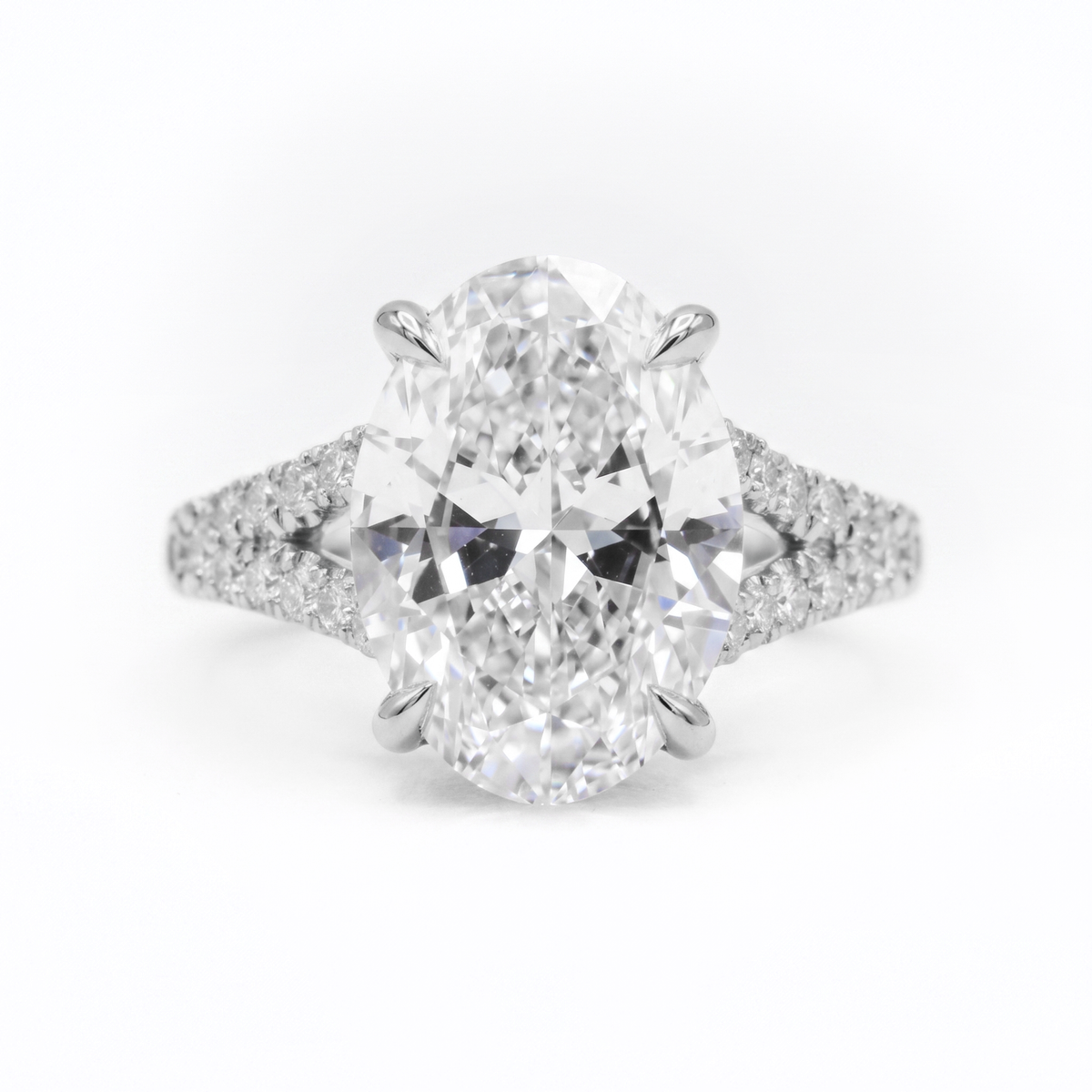 An oval cut diamond engagement ring with a brilliant solitaire center stone and pavé set diamond shoulders on a white background