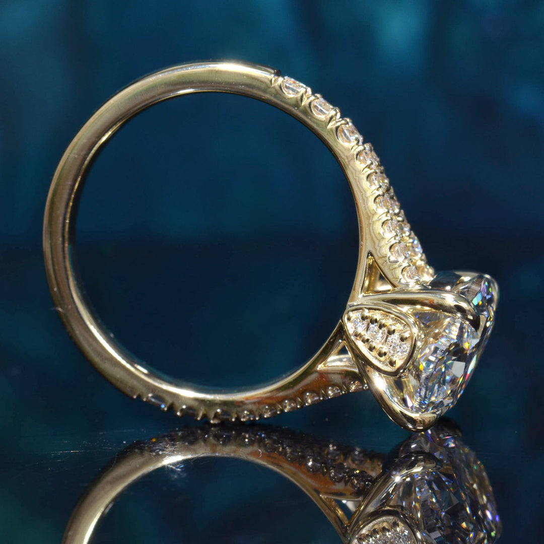 A yellow gold ring featuring a large clear round-cut gemstone in a decorative setting with smaller accent stones along the band, photographed on a dark blue reflective surface.