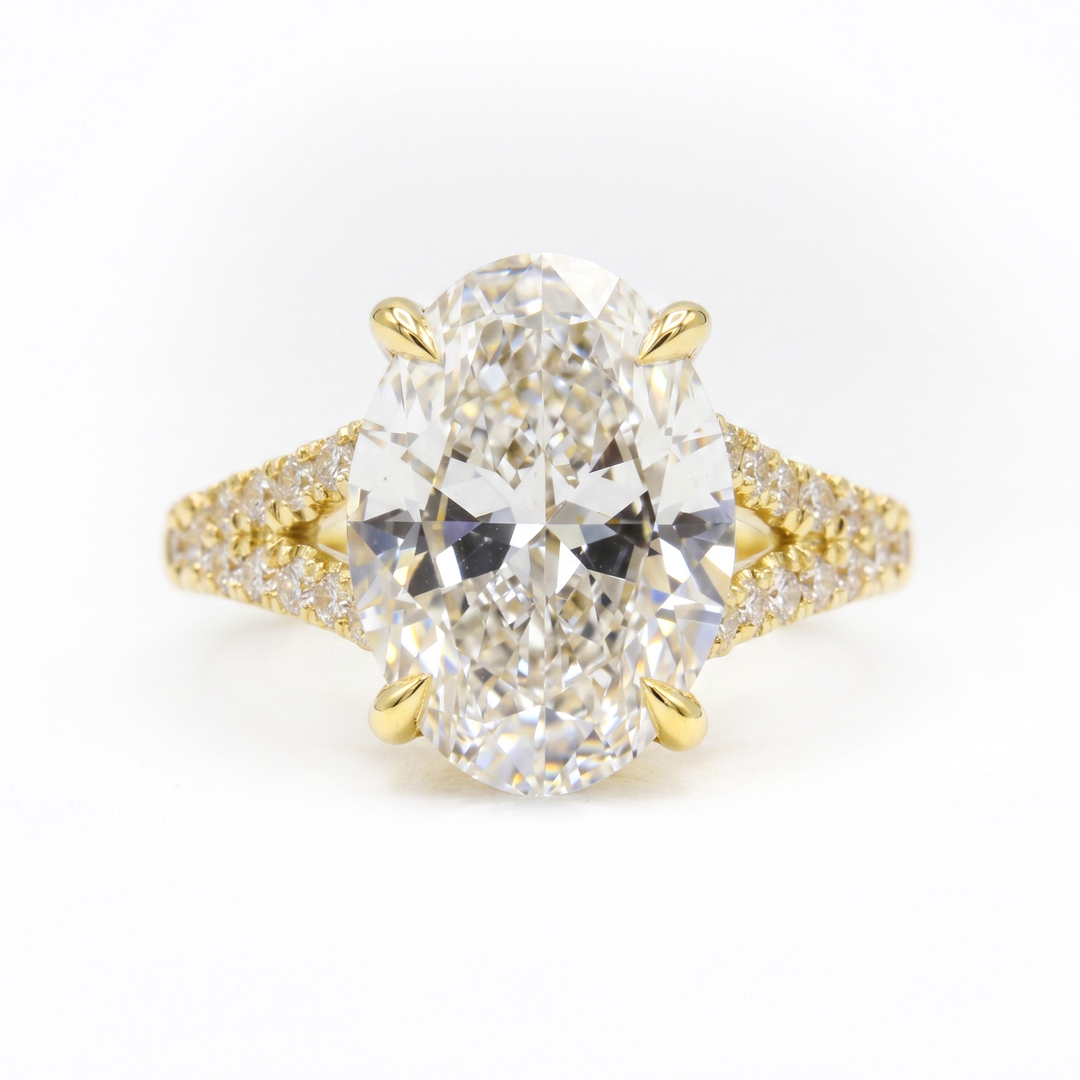 An oval diamond engagement ring with a yellow gold prong setting and a diamond-paved band, shown on a clean white background.