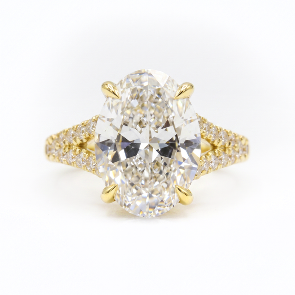 An oval diamond engagement ring with a yellow gold prong setting and a diamond-paved band, shown on a clean white background.