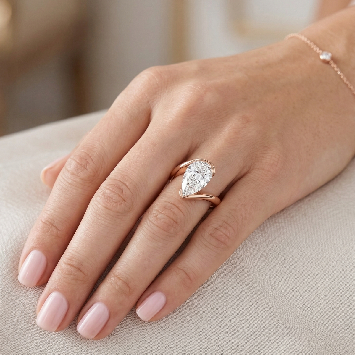 Pear cut diamond solitaire bypass ring in rose gold on model's ring finger