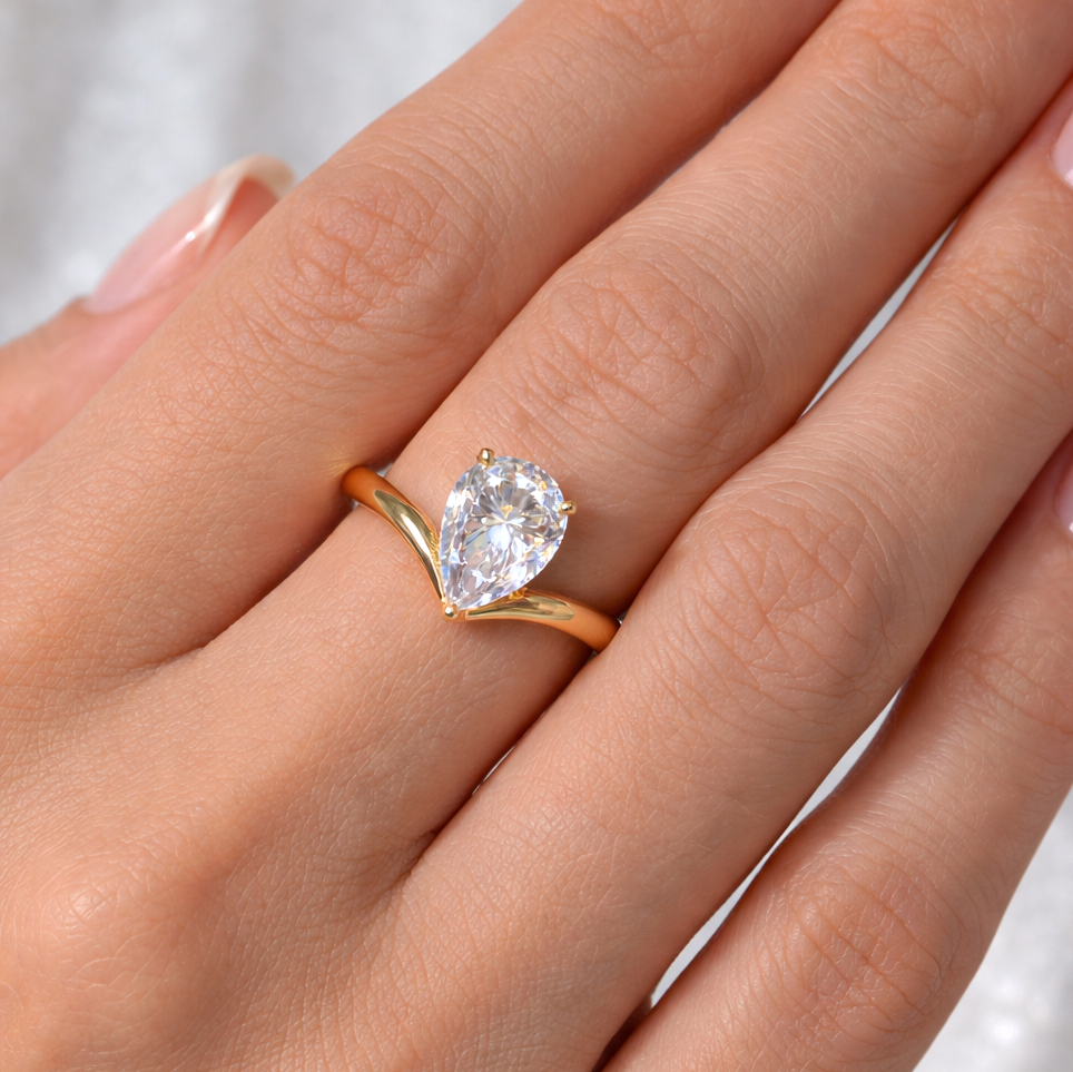 Pear cut chevron solitaire engagement ring in yellow gold worn on model's 3rd finger
