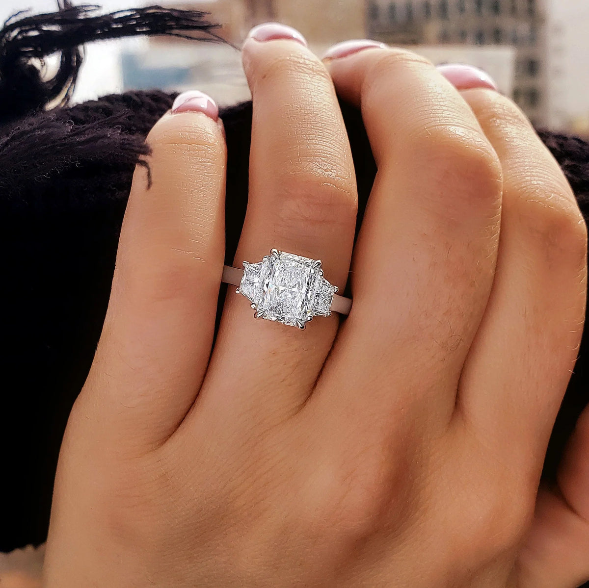 Elongated radiant cut center with trapezoid side 3 stone diamond ring in white gold on model's ring finger