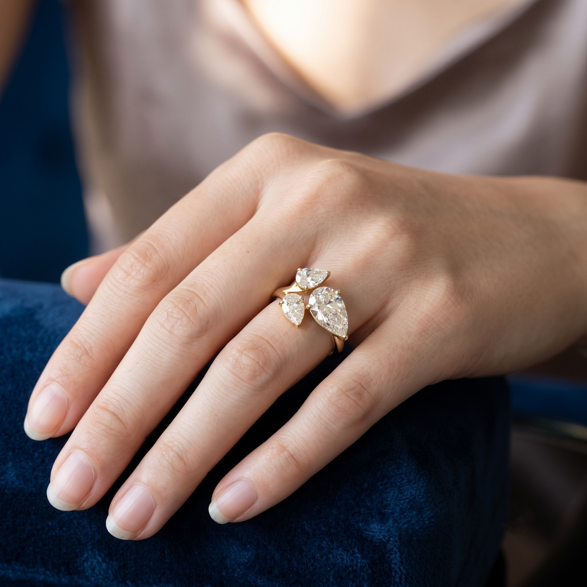 A close up of a hand wearing a gold ring with three marquise cut clear gemstones, resting on a dark blue velvet surface