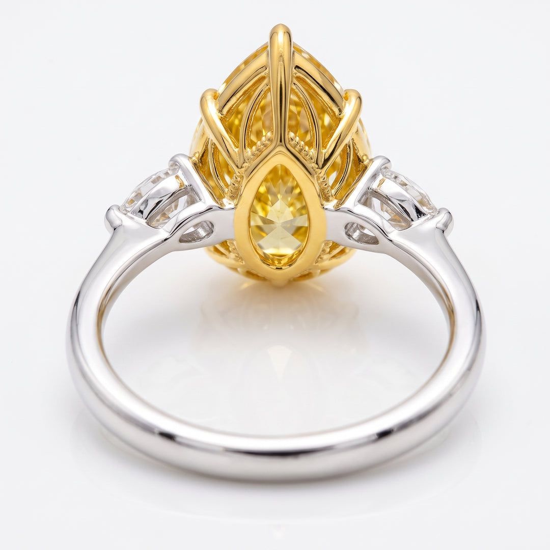 A two-tone yellow gold and white gold ring featuring a large teardrop-shaped yellow center stone, flanked by smaller side stones on a polished white gold band, shown on a white background.
