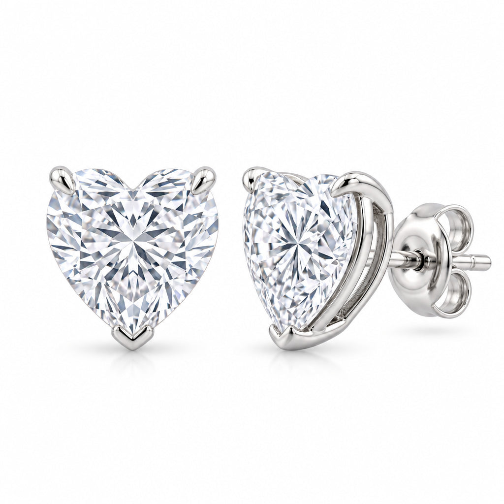 A pair of heart-shaped diamond stud earrings in silver-colored metal, shown from both front and side angles on a light gray reflective surface.