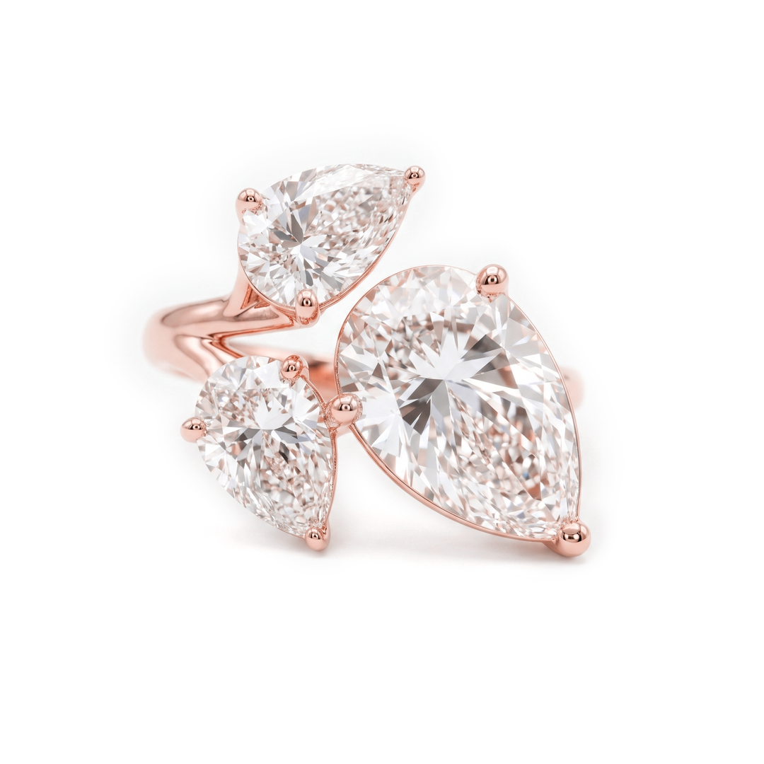 Rose gold ring with three pear-cut clear gemstones in a clustered setting, photographed on a clean white background.
