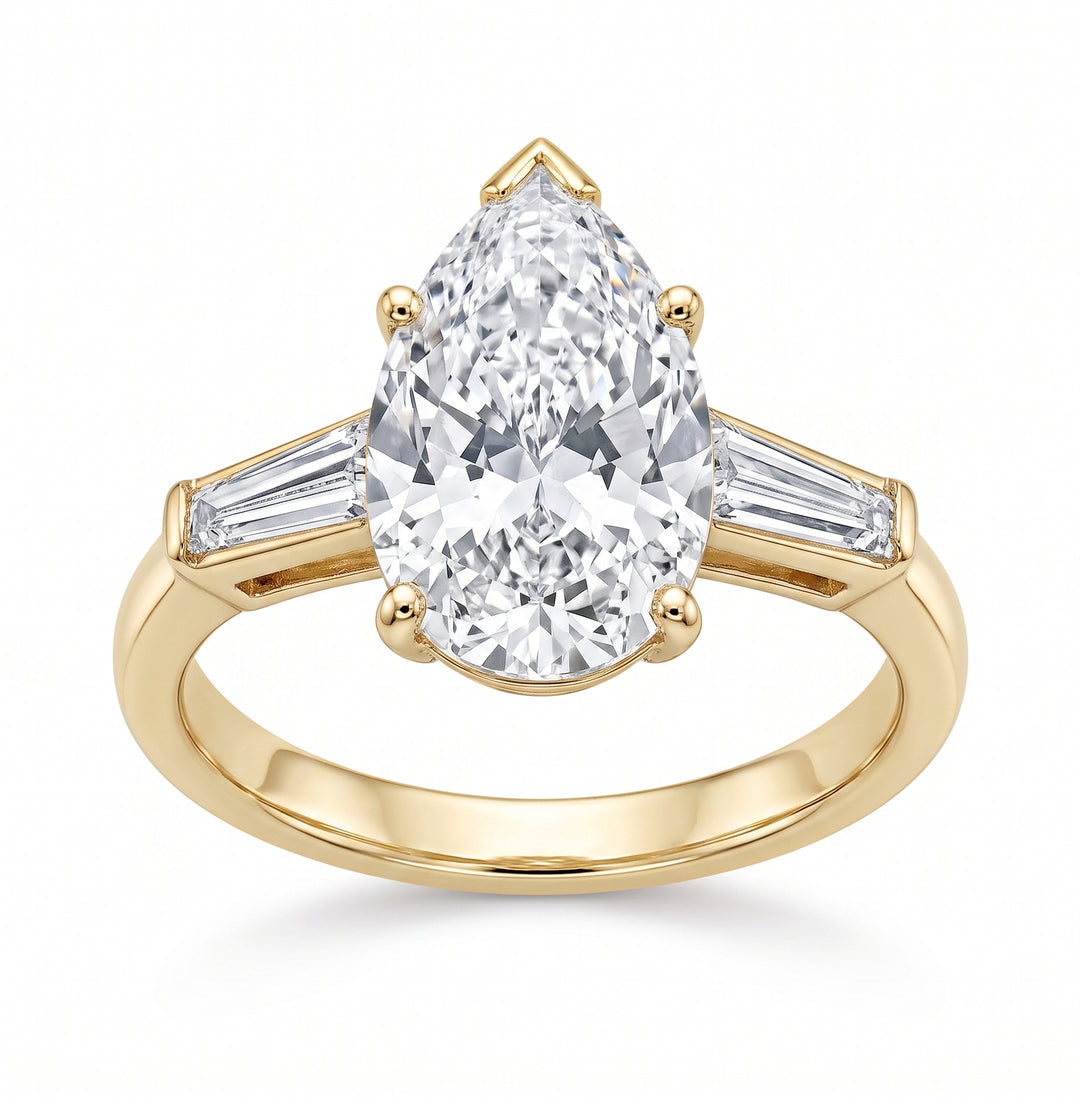 A yellow gold ring featuring a large pear-cut center stone with baguette side stones, shown on a clean white background.