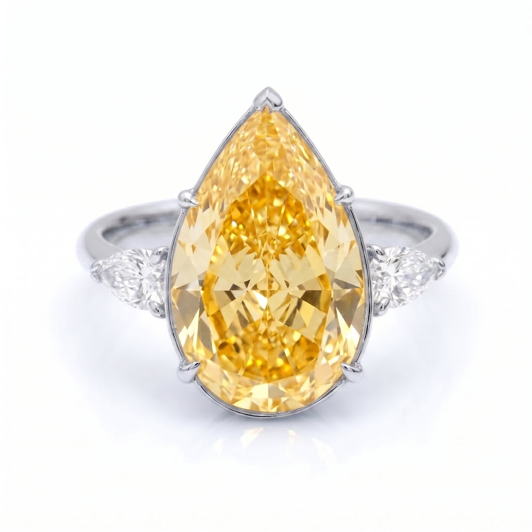 A pear-cut yellow diamond ring set in a white gold band with small pear cut diamonds on either side, shown on a clean white background.