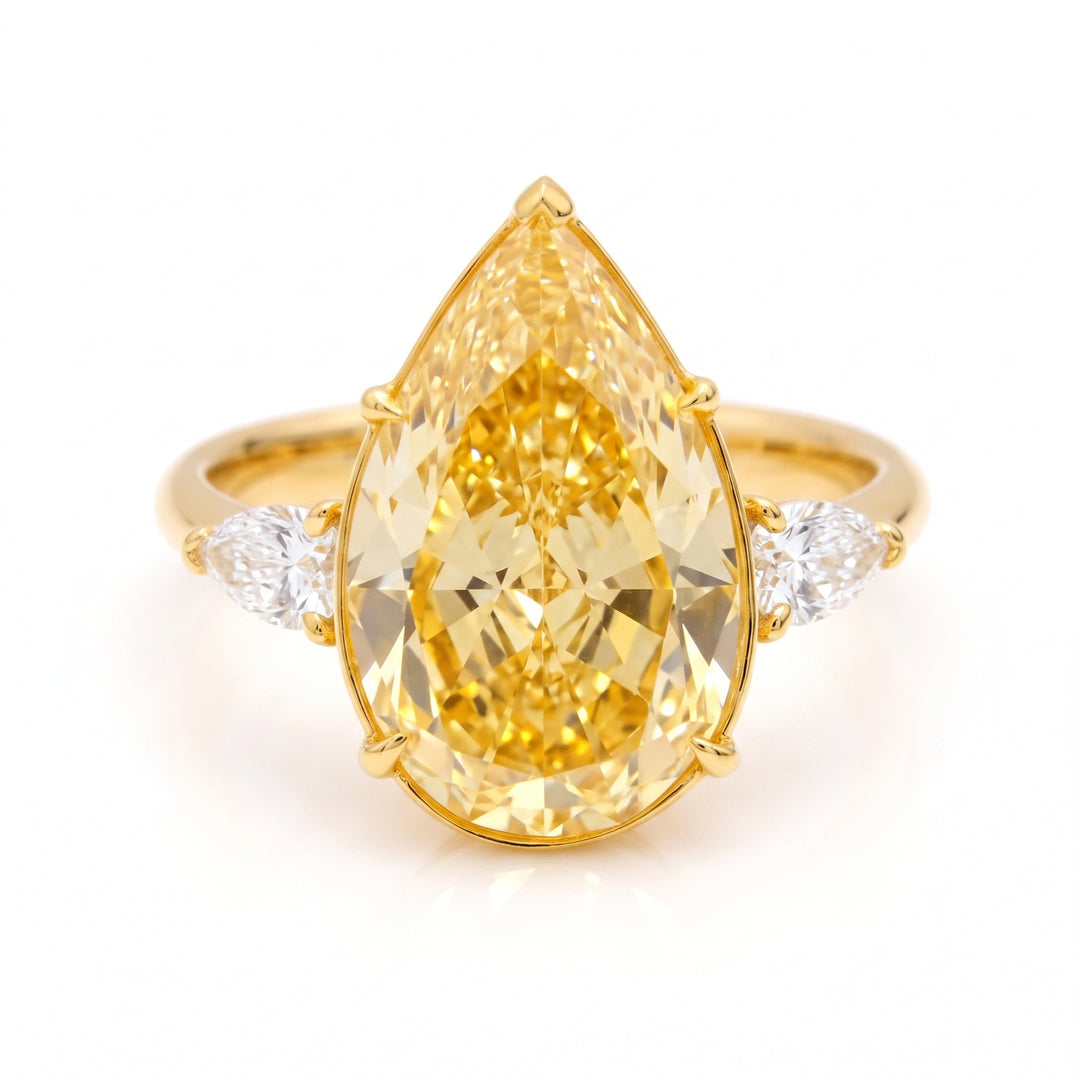 A yellow gold ring featuring a large pear-cut yellow diamond center stone with two small round diamonds on either side of the band, set against a clean white background.