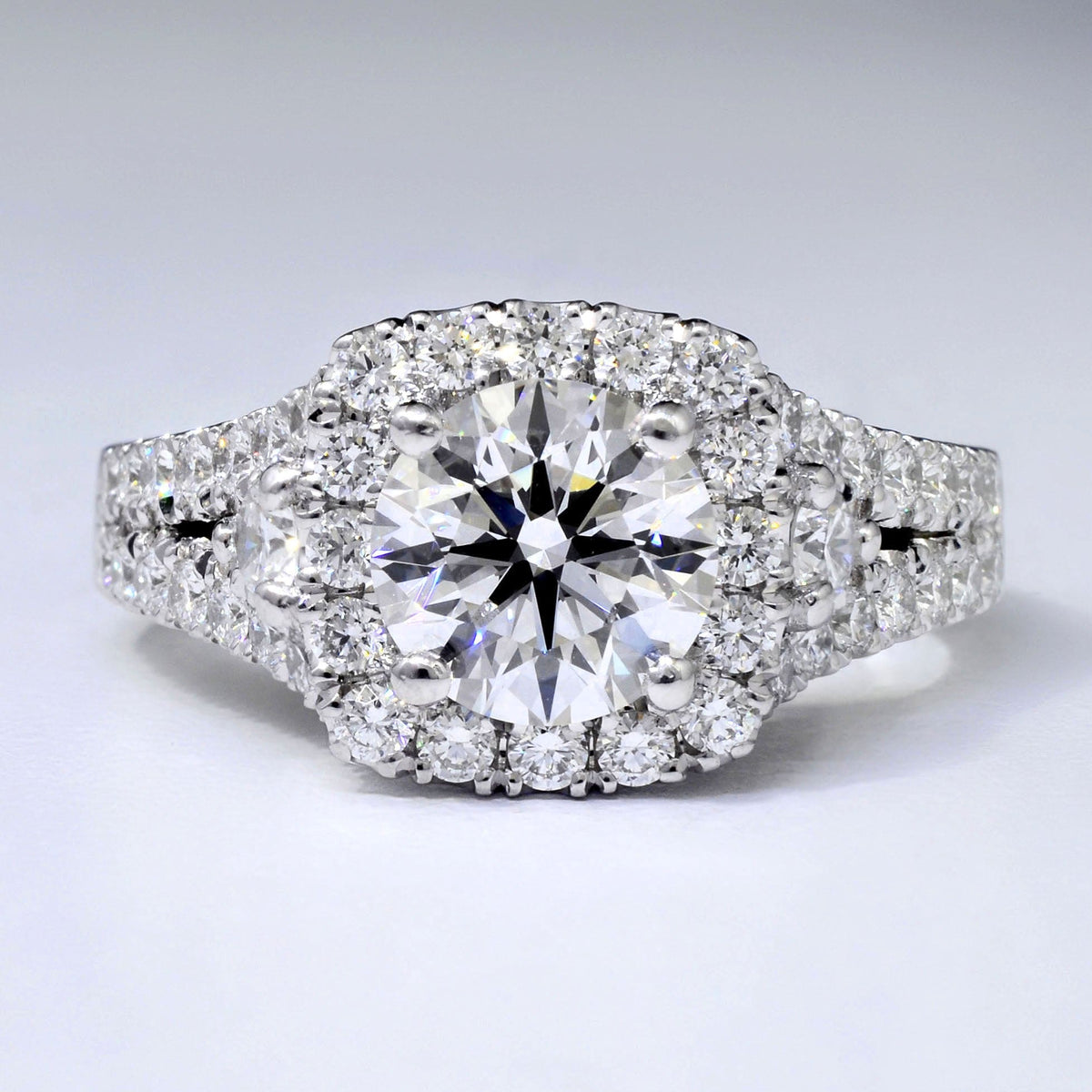 A round cut engagement ring with a cushion halo design, set in a pavé setting, adorned with smaller round cut diamonds across the band
